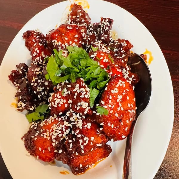 Pakistani chili chicken with sesame seeds and cilantro on a white plate with a spoon.