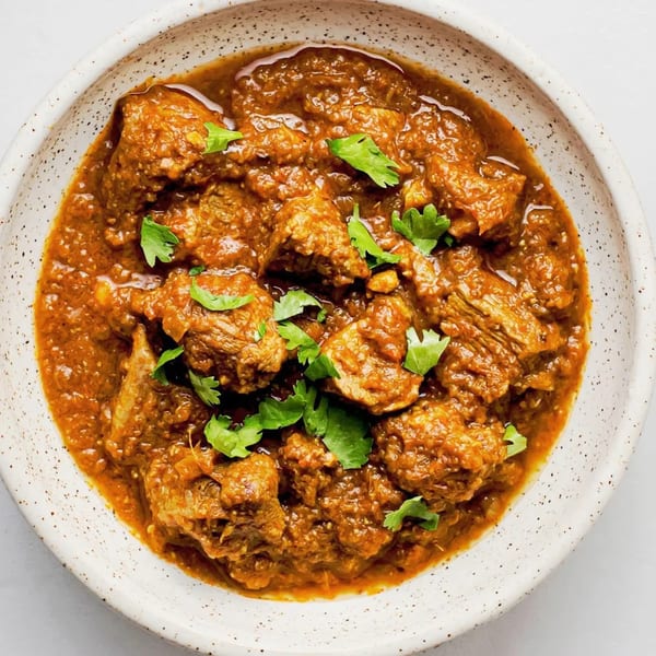 A close-up of a Pakistani lamb or beef karahi, garnished with fresh cilantro in a white bowl.