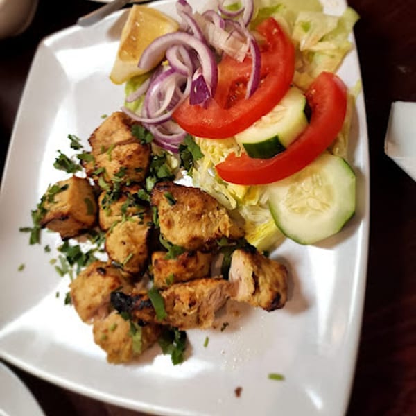 Pakistani chicken tikka with fresh salad, red onions, tomatoes, cucumbers, and a lemon wedge.