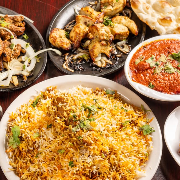 A spread of Pakistani dishes including biryani, chicken tikka, seekh kabab, and butter chicken.