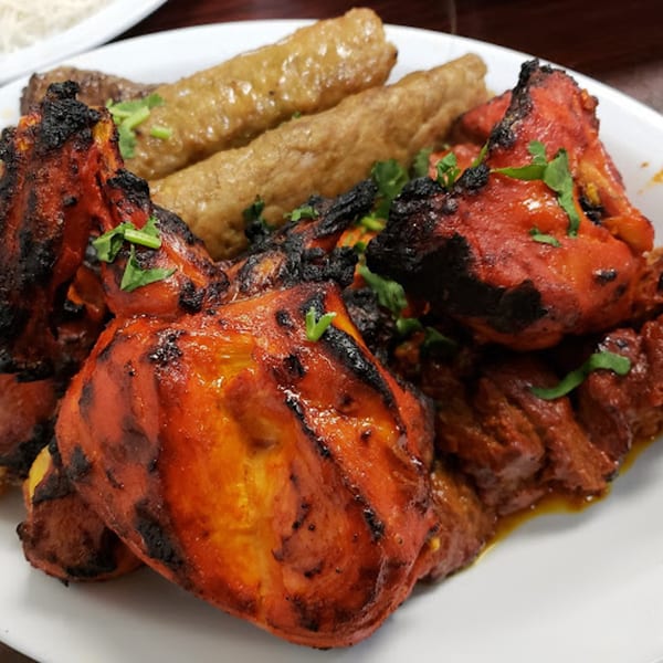 A plate of Pakistani food with charred red chicken tikka and two brown seekh kabobs, garnished with cilantro.