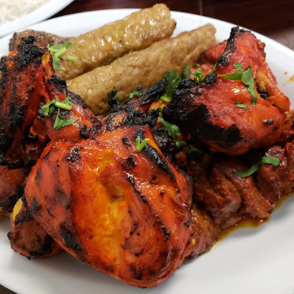 A plate of Pakistani food with charred red chicken tikka and two brown seekh kabobs, garnished with cilantro.